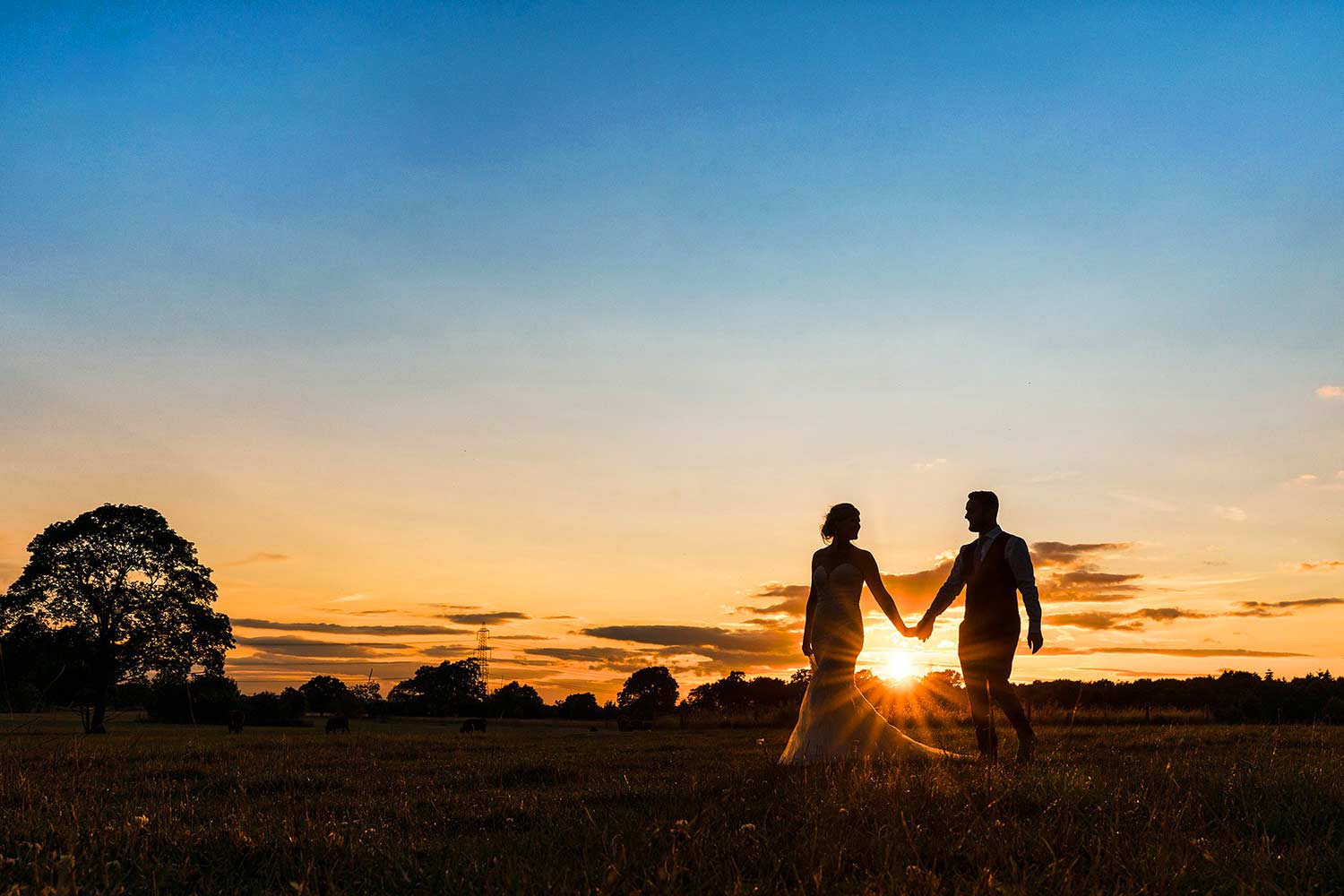 Bride and groom walking hand in hand with the sunset directly behind them