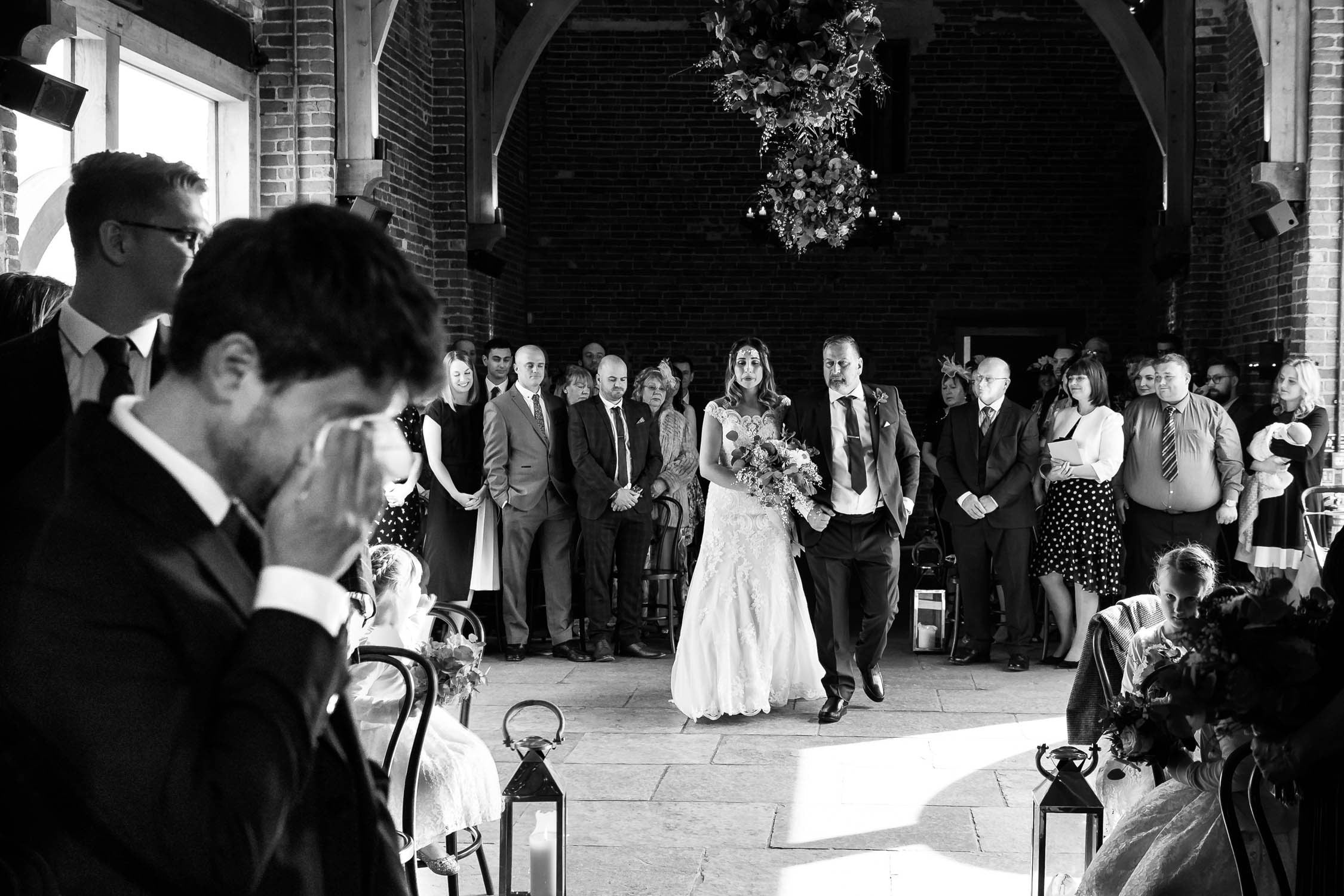 Bride walking down the aisle at Hazel Gap Barn as groom wipes away a tear
