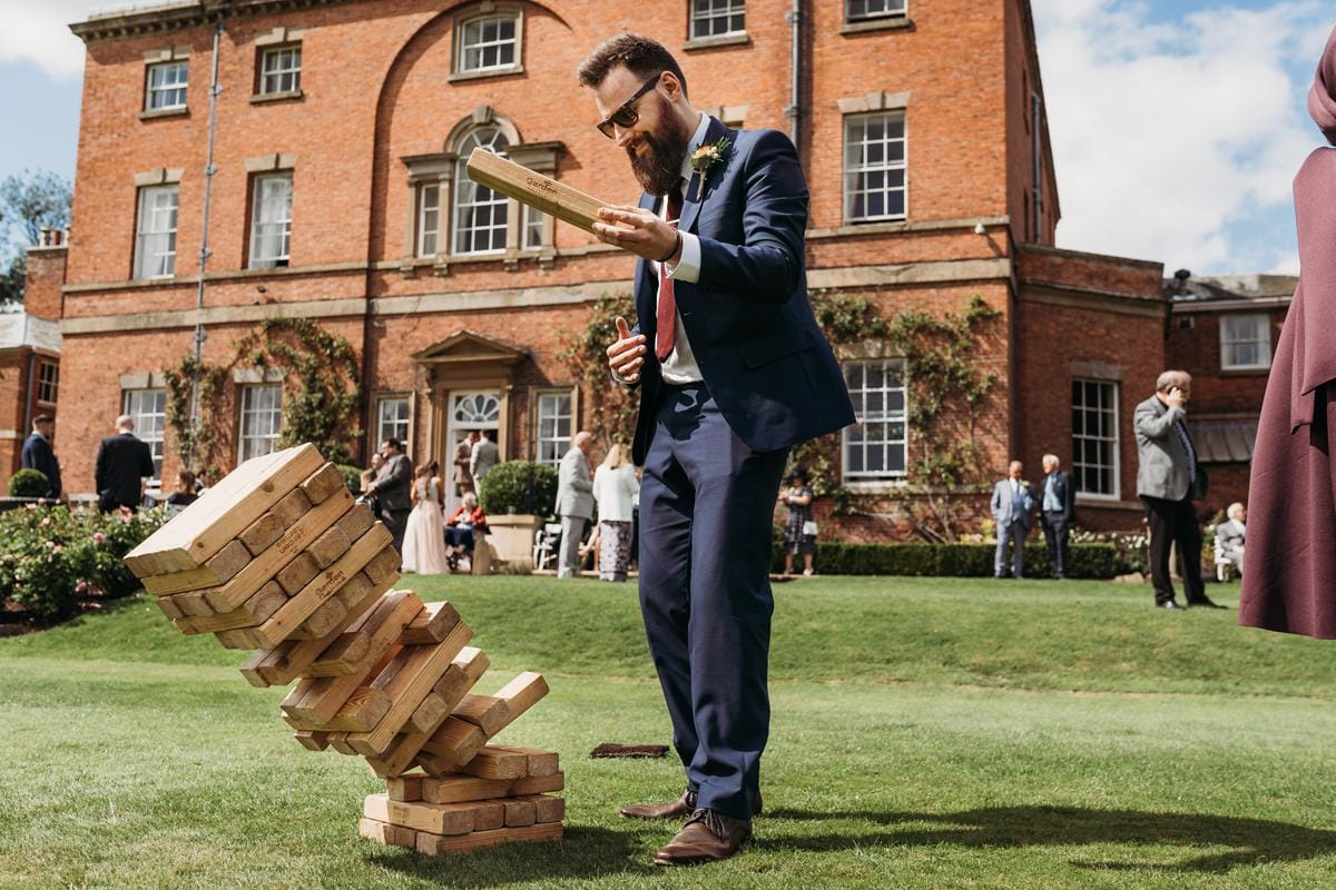 Wedding guest putting a block onto the top of a giant Jenga block as it falls. Norwood Park is in the background