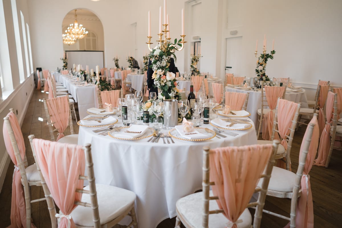 The Gallery room all set up for a wedding breakfast with tables decorated with candles and coral coloured chair covers and sashes