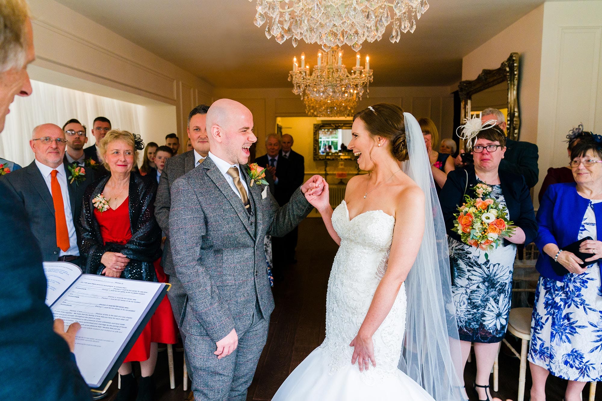 A wedding photo taken at Old Vicarage in Nottingham of the Bride and groom cheering just after the registrar prounounces them husband and wife, whilst their friends and family look on. Mother of bride's face is red from all the crying during the ceremony.