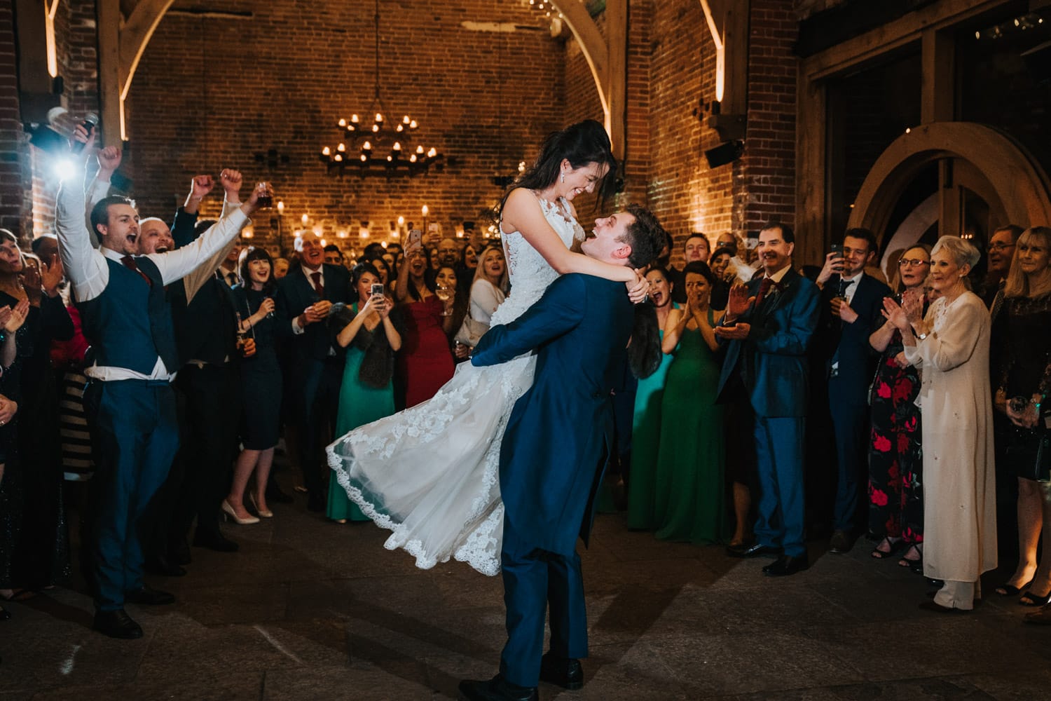 Groom lifts bride up for a spin during first dance at Hazel Gap Barn whilst guests cheer