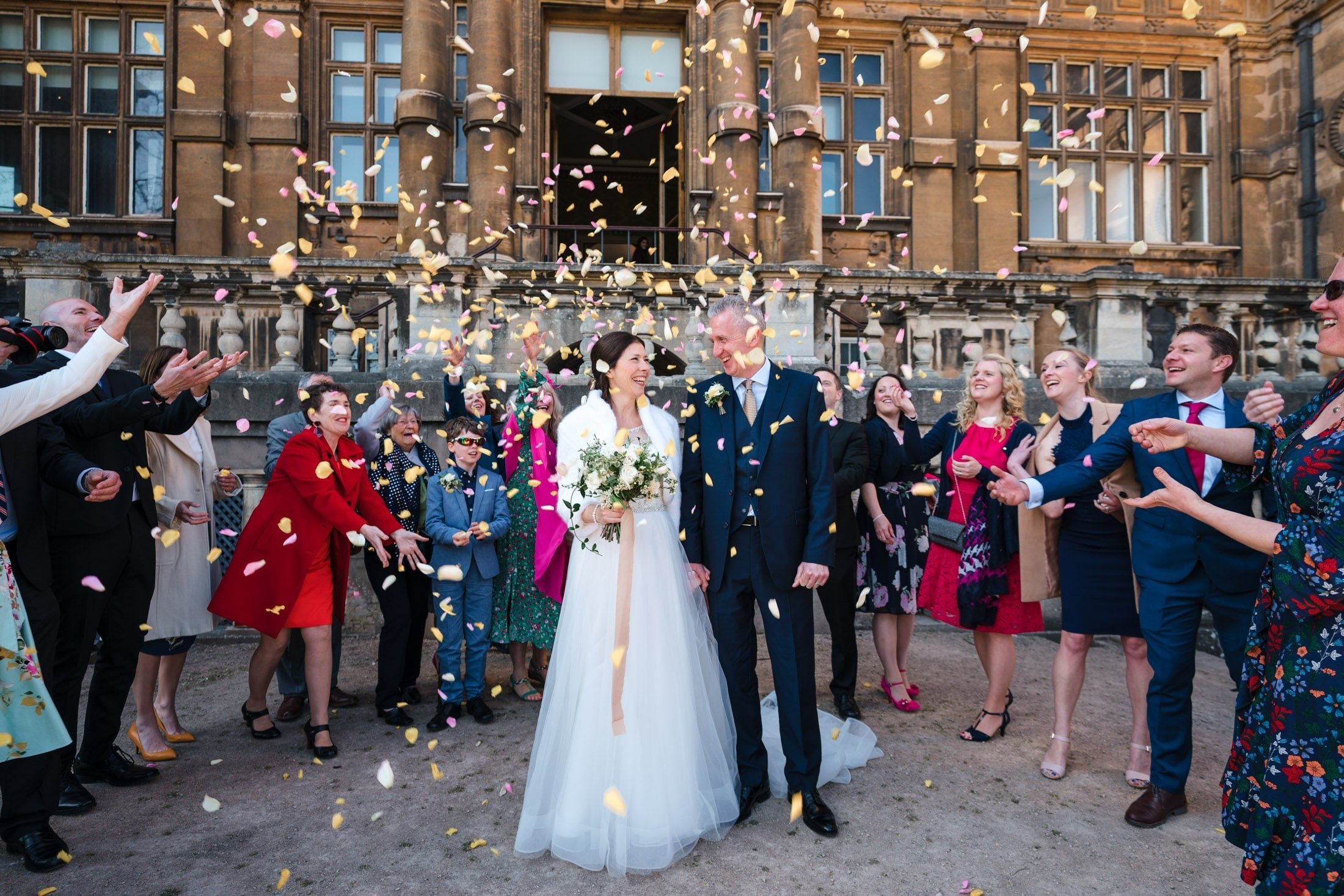 Guests throwing confetti over bride & groom outside Wollaton Hall in Nottingham