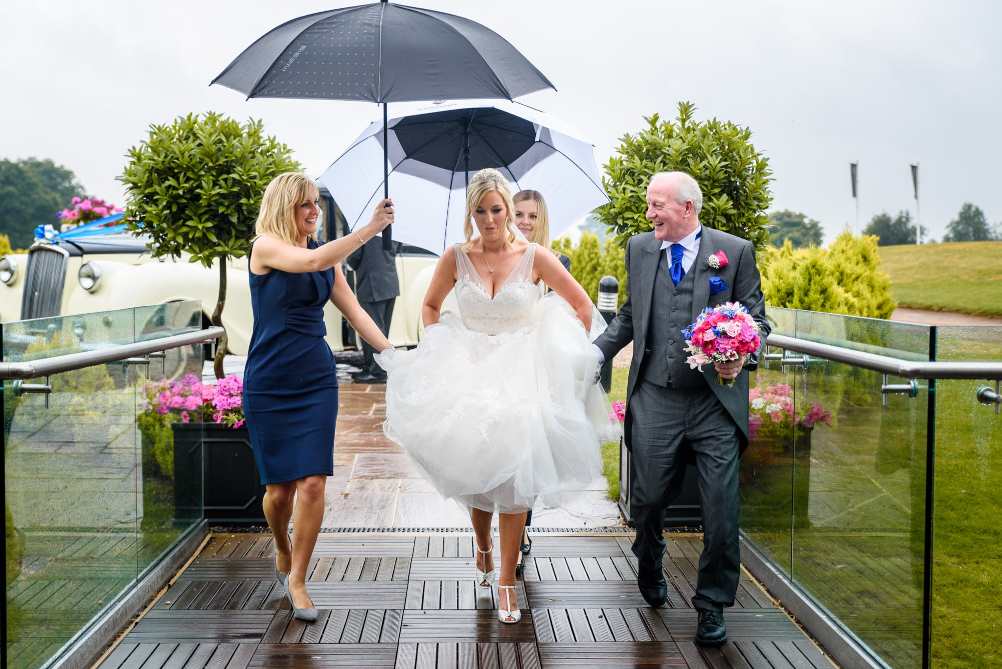 Bride walks into the ceremony in the rain with planner holding umbrella over her