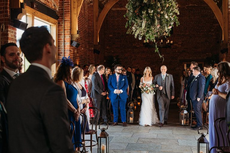 bride walking down the aisle with her father at Hazel Gap Barn with her friends and family smiling at her