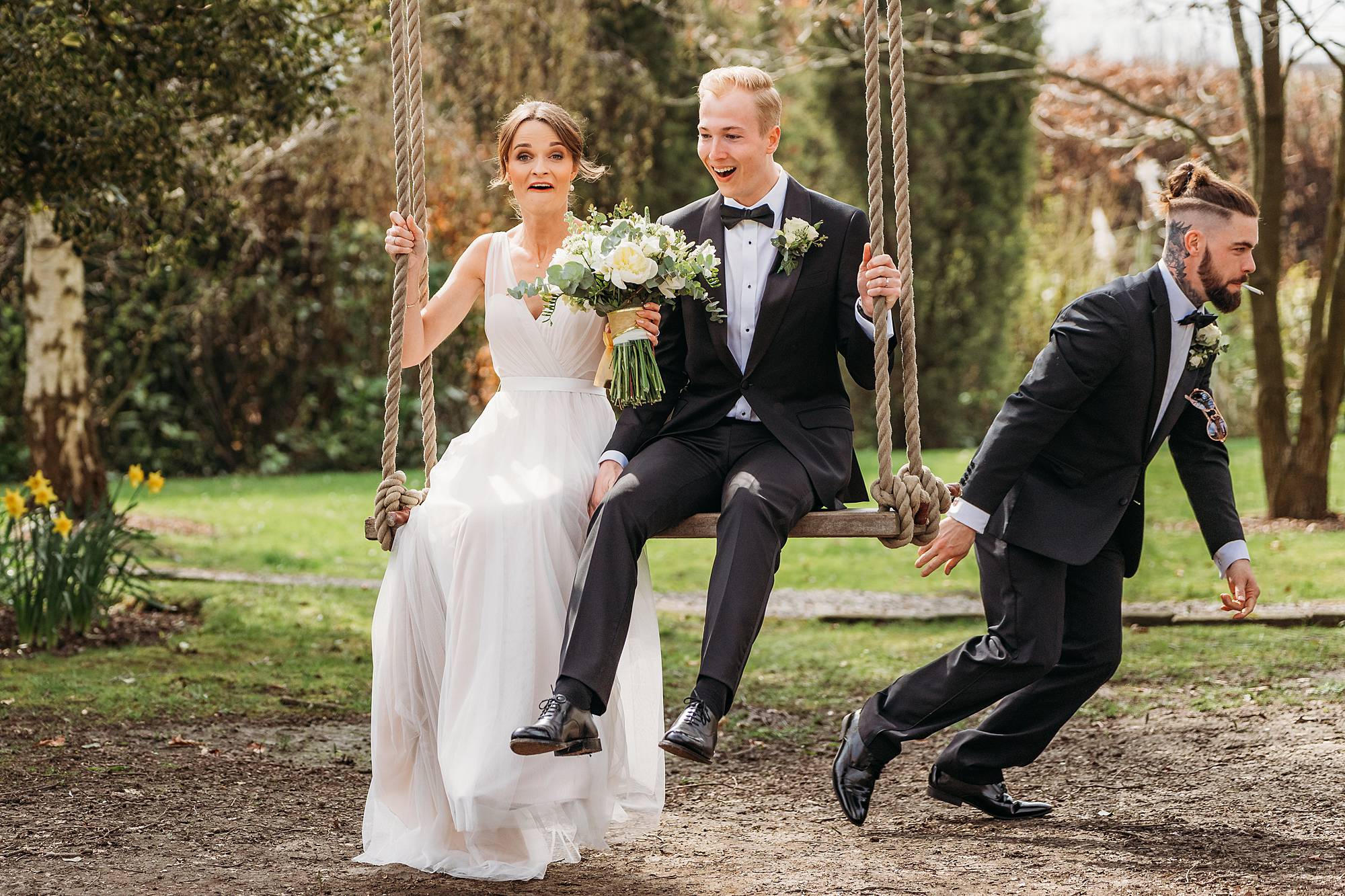 Bride looking worried as she is being pushed on the swing by the best man as he runs away with a cigerette in his mouth