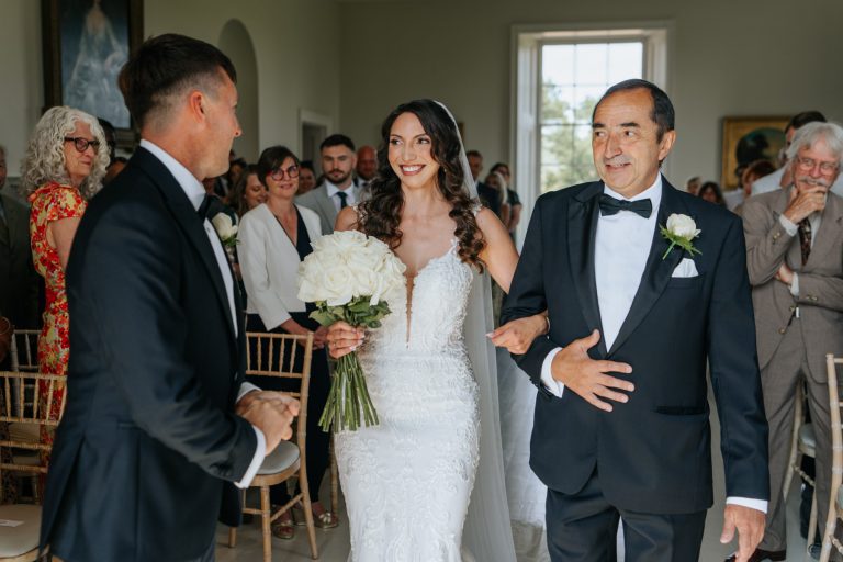 Bride smiling with dad as she greets groom at the end of the aisle in the music room at Stubton Hall