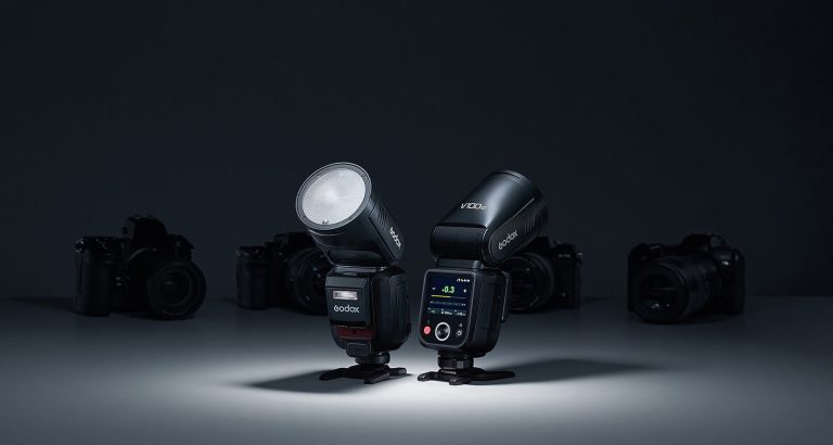 Godox V100 flash front and back on a dark background with cameras in the background